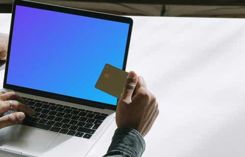 MacBook user holding a debit card in hand mockup.
