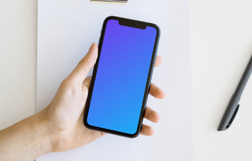 iPhone mockup in a user’s hand over a note pad and a cork