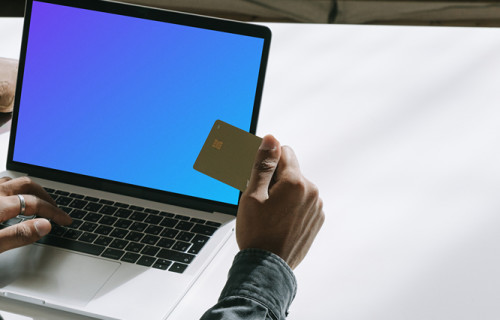 MacBook user holding a debit card in hand mockup.