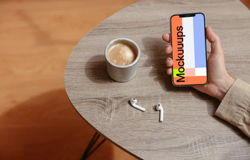 Simple handheld iPhone mockup held on the table with a pair of Airpods at the side