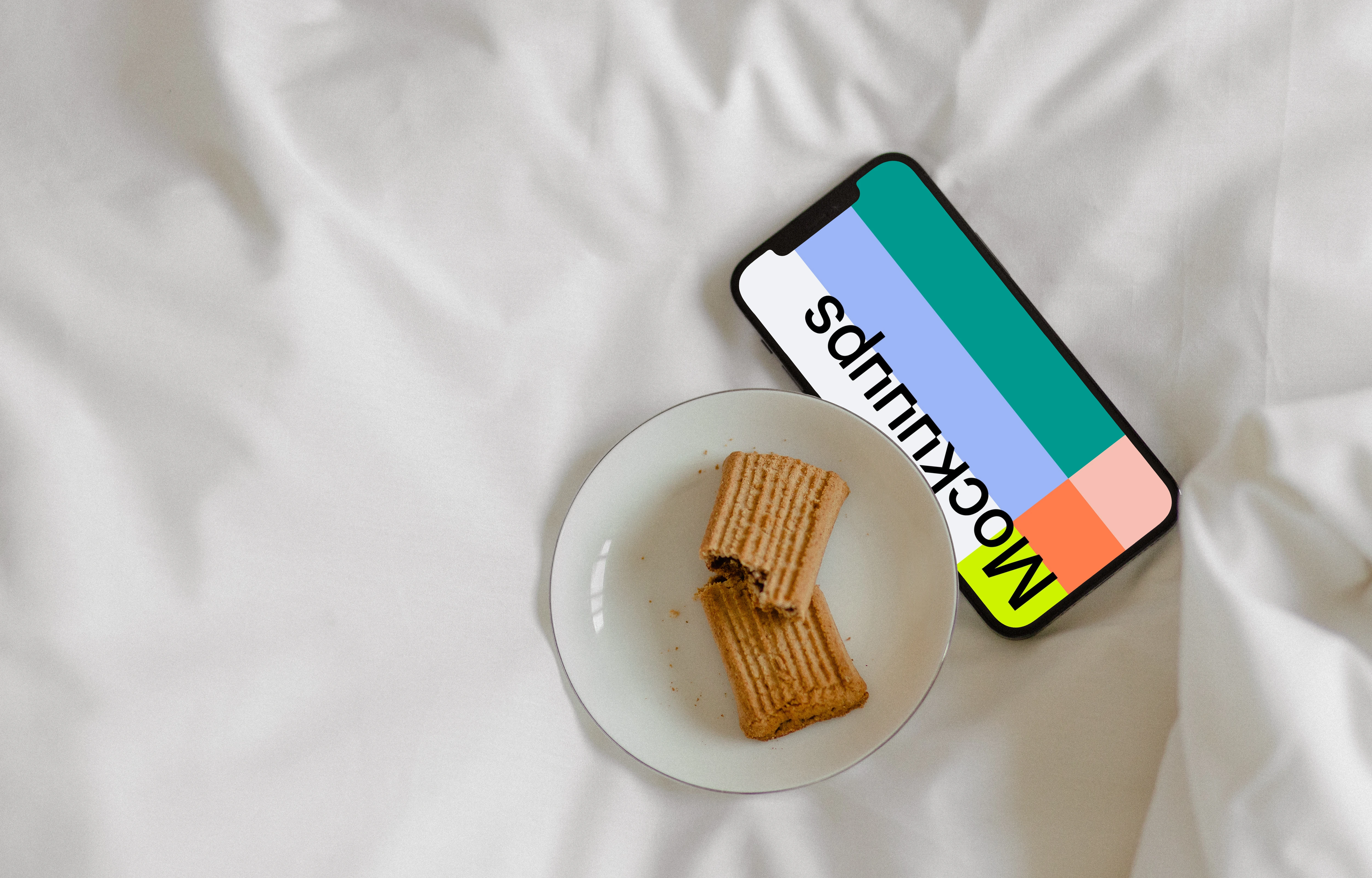 iPhone 12 Pro mockup on bed with a plate of biscuits