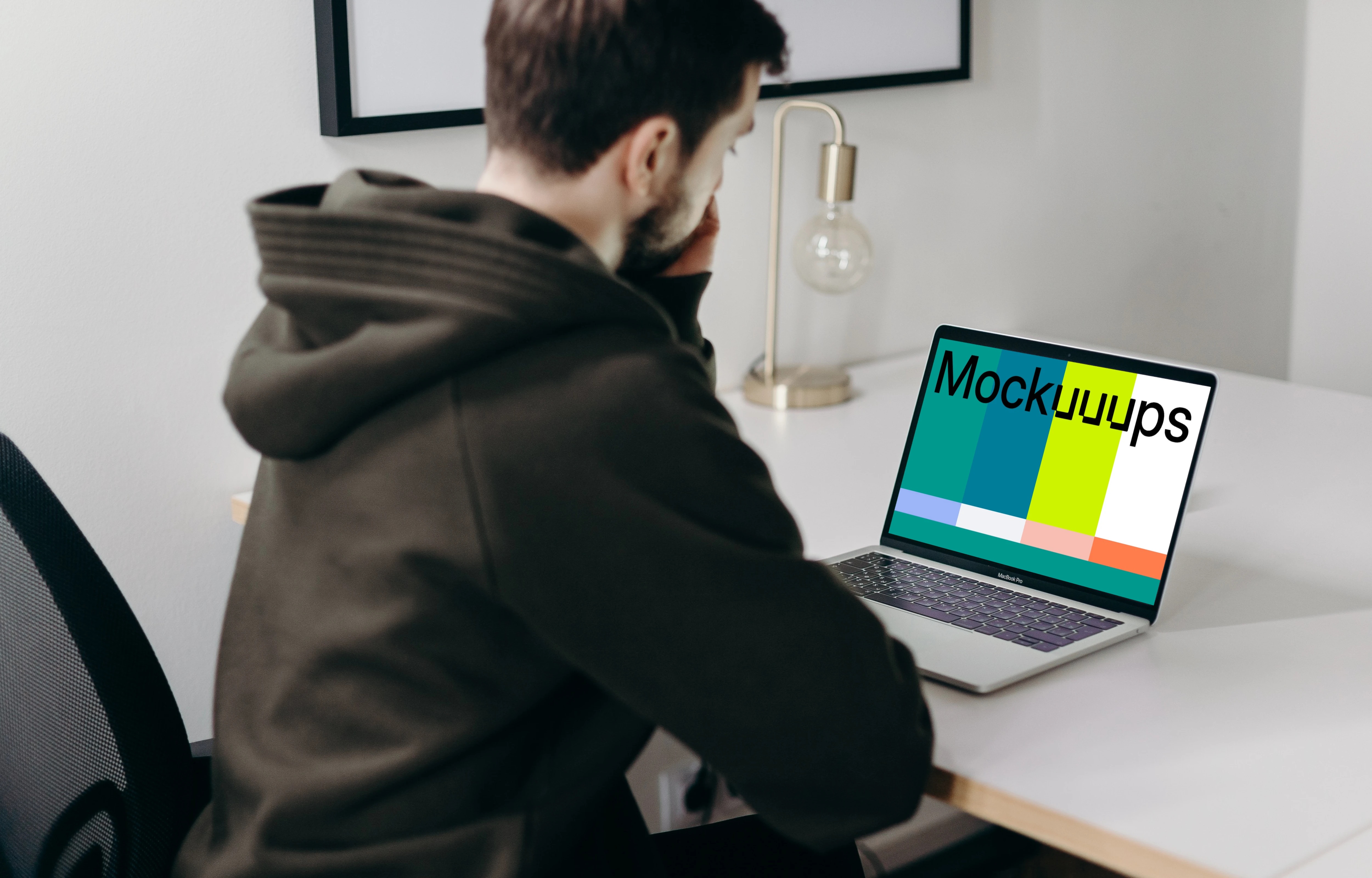 MacBook Pro mockup on a white table being used by a man in a black hoodie