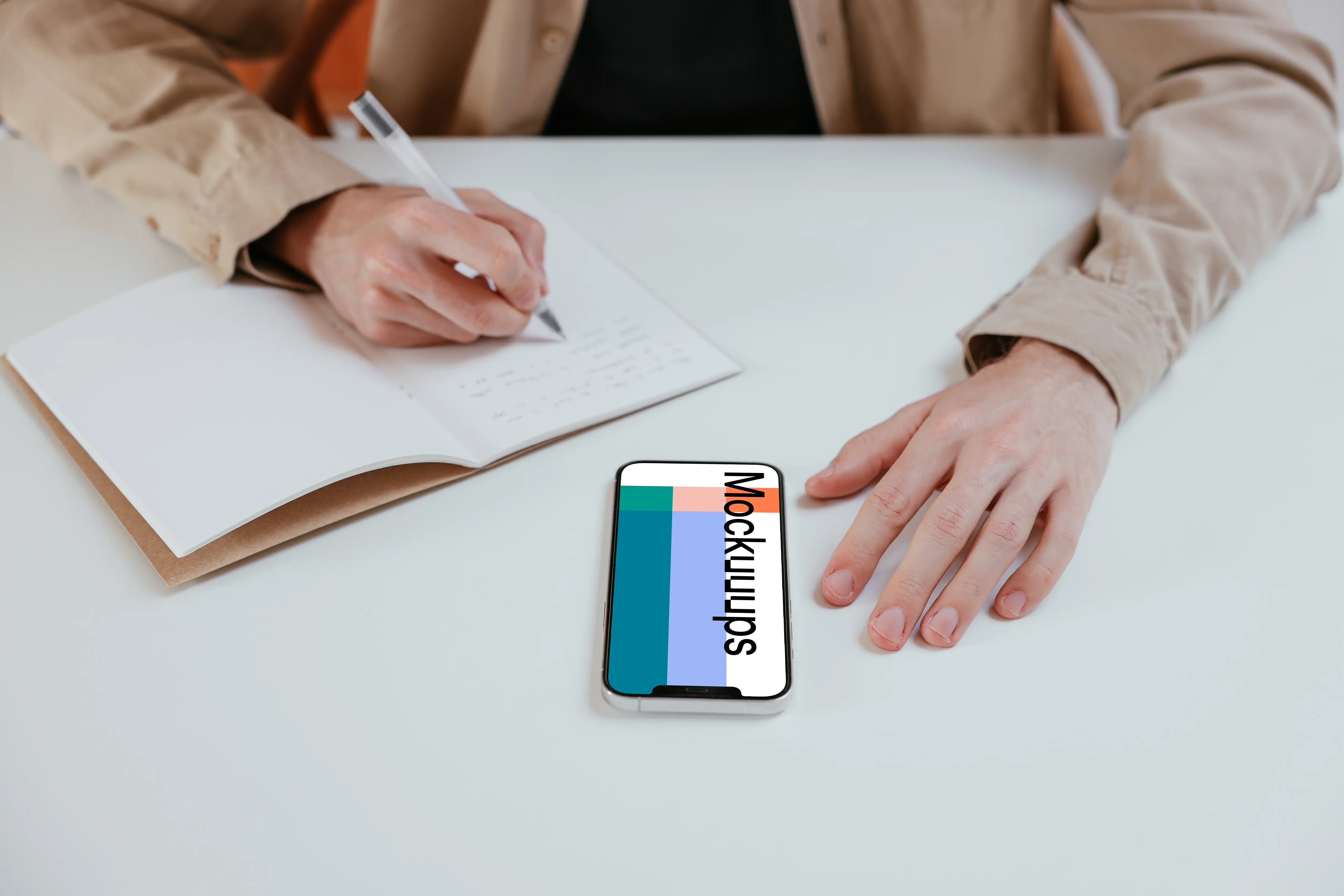 iPhone mockup on a white table next to a notebook 