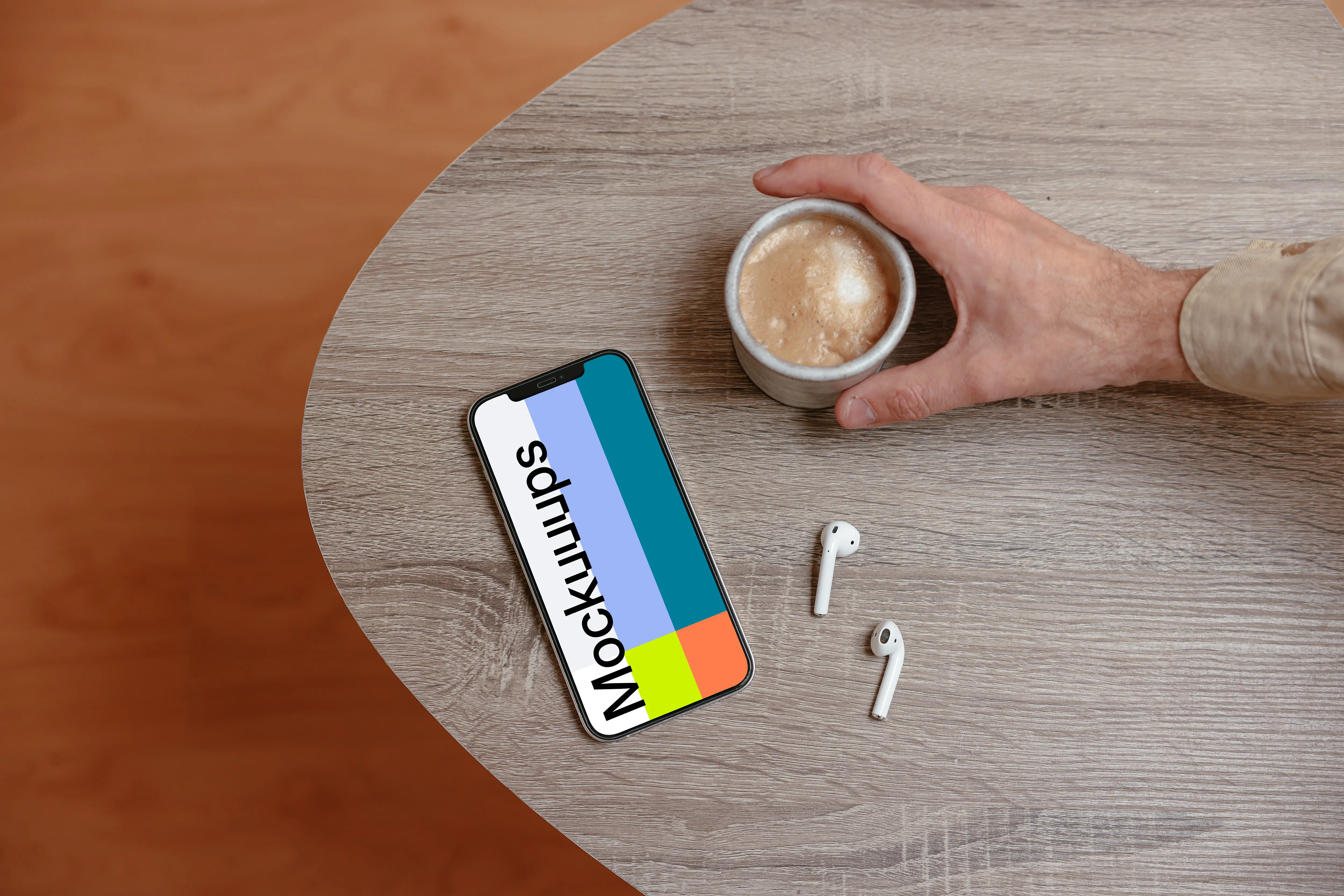 iPhone mockup on a wooden table next to a cup of coffee and a pair of AirPods.