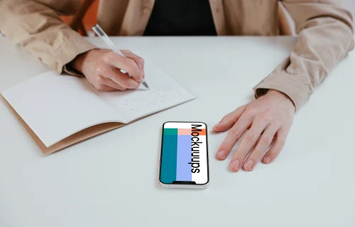 iPhone mockup on a white table next to a notebook 