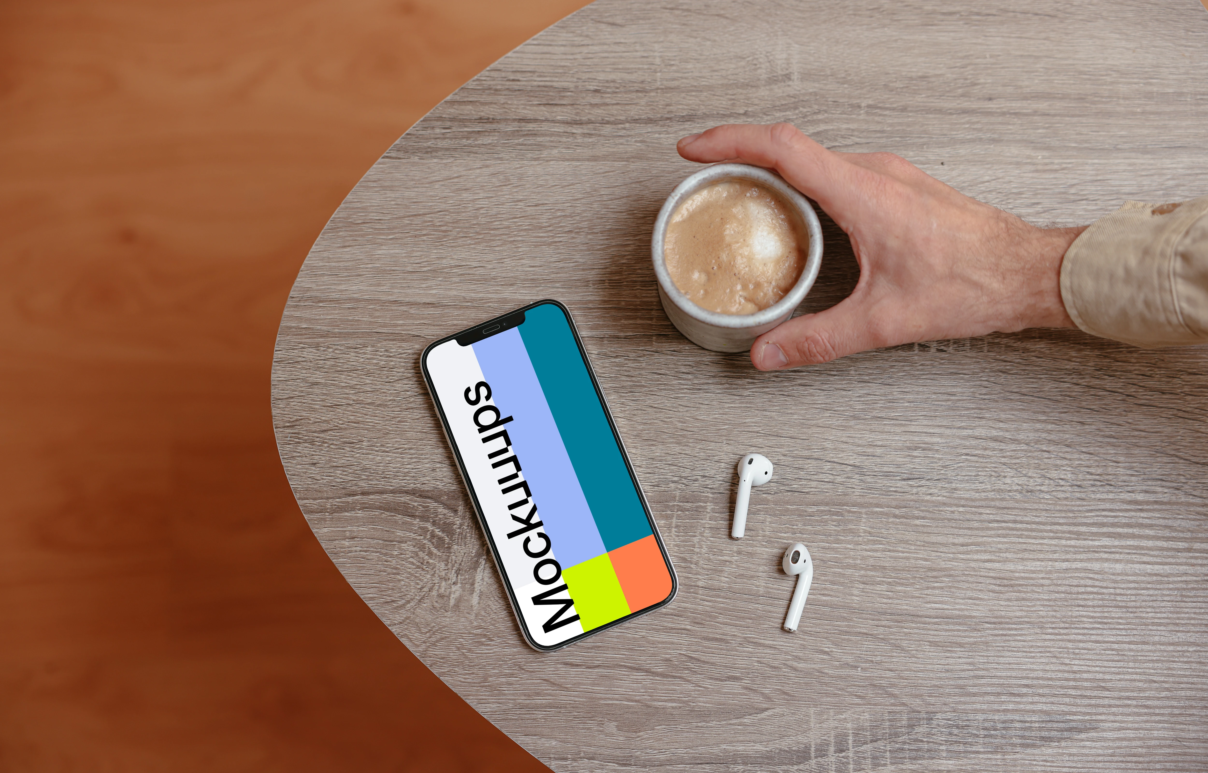 iPhone mockup on a wooden table next to a cup of coffee and a pair of AirPods.