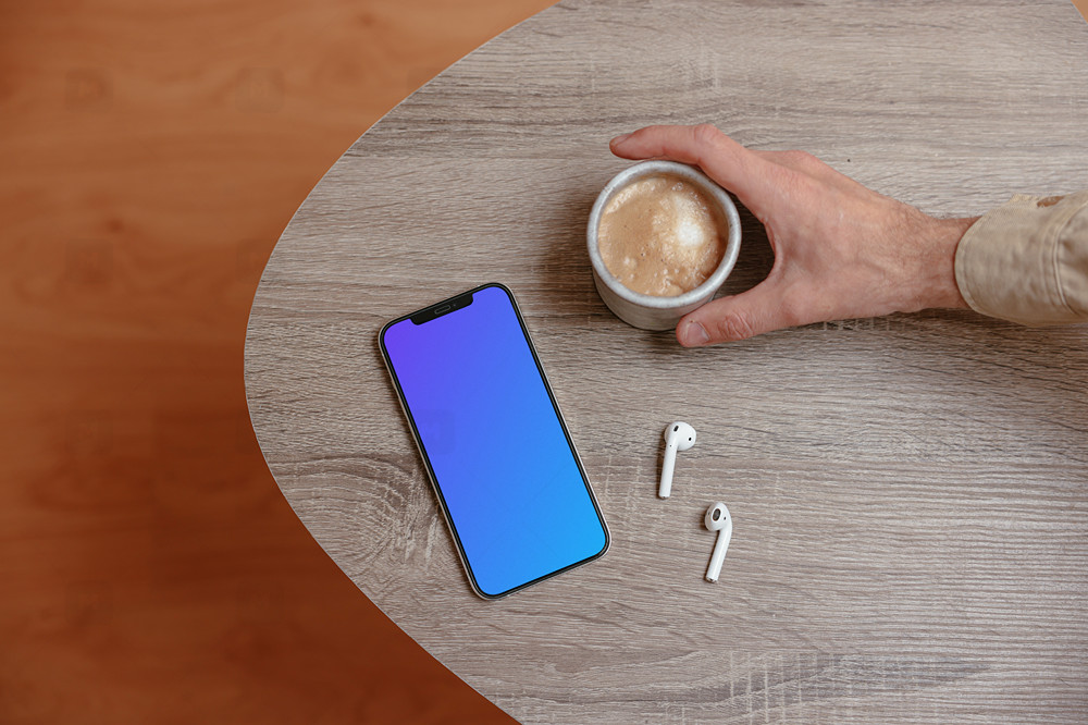 iPhone mockup on a wooden table next to a cup of coffee and a pair of AirPods